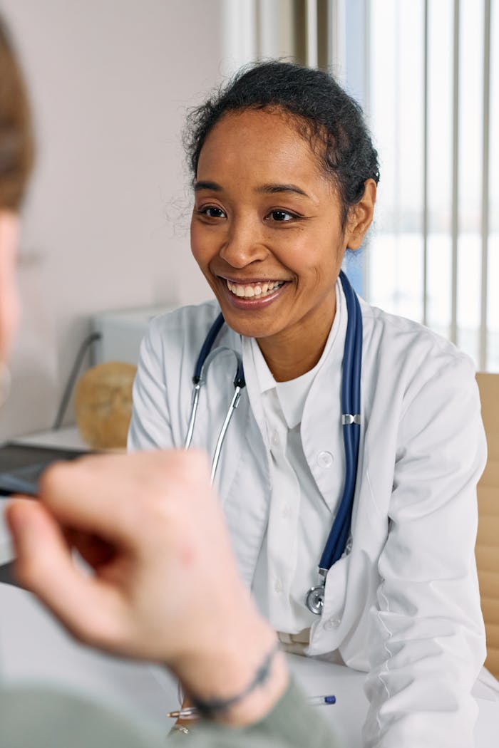 A smiling doctor in a white coat with a stethoscope provides a warm consultation.